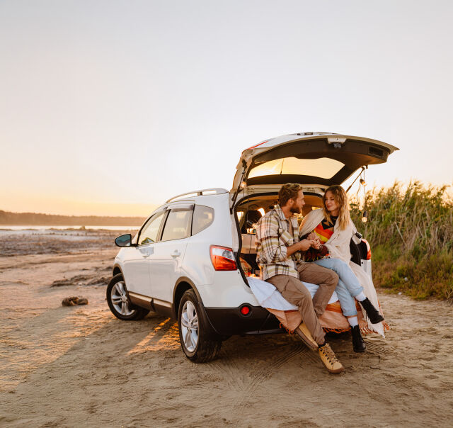 Et par som sitter bak i bilen på en strand