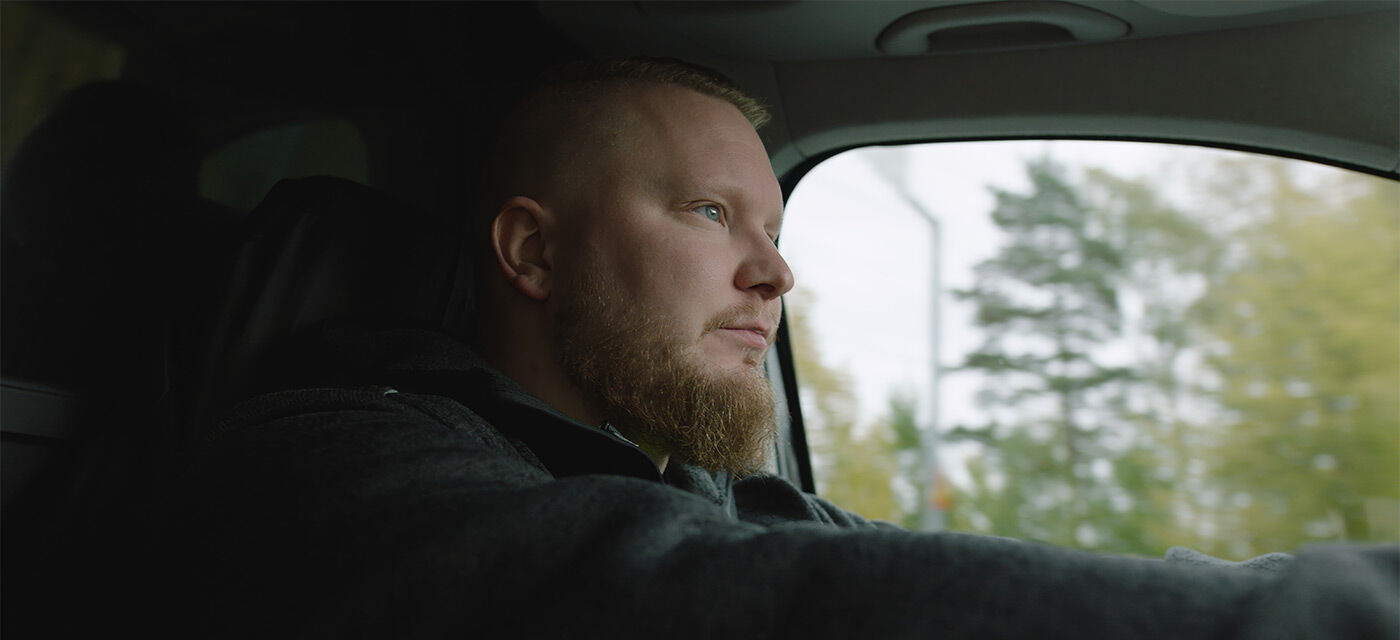 Pakettiautoa kuljettava mies kuvattuna apukuljettajan suunnasta läheltä kasvoja