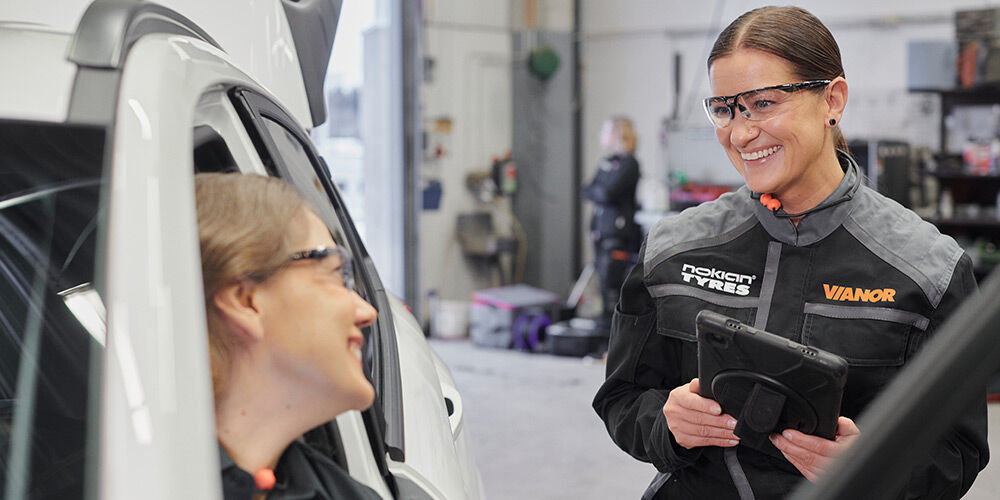 To av Vianors bilmekanikere ser smilende på hverandre. Den ene sitter i førersetet og den andre utenfor bilen. 