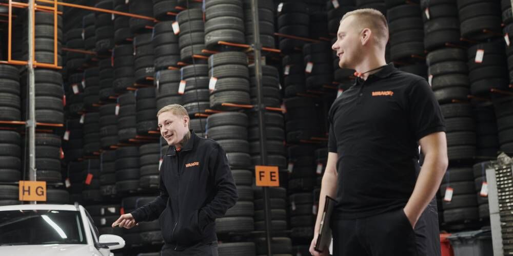 Mekanikere fra Vianor diskuterer bilservice foran stablede bildekk i dekkhotell.