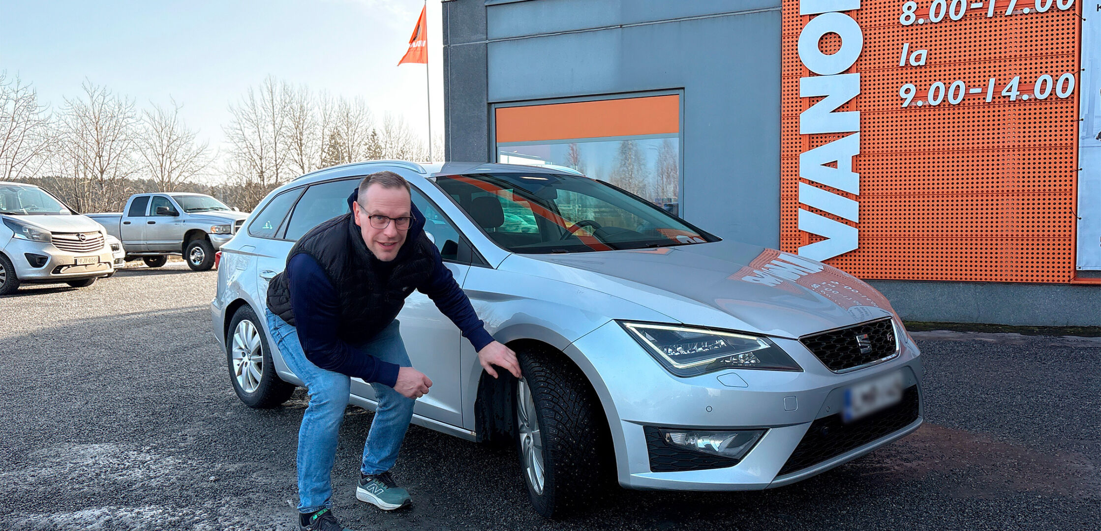Ville Nieminen kyykistyy hopeanvärisen auton vieressä ja koskettaa eturengasta Asiakas Ville Nieminen istuu oranssilla sohvalla kahvikuppi kädessään Vianorin palvelupisteen odotustilassa. Vianorin palvelupisteen ulkopuolella. 