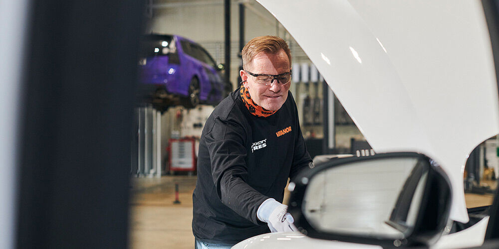 Vianor-mekaniker sjekker bilbatteriet med bilens hvite panser foran på bildet