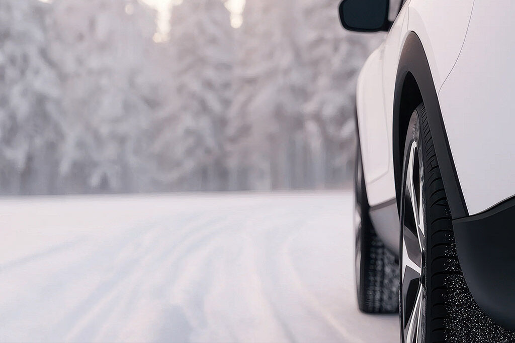 Skoda Enyaq-elbilens vinterdekk på en snødekket vei. Bilens bakdekk er synlig i nærbilde, med et vinterlandskap i bakgrunnen.