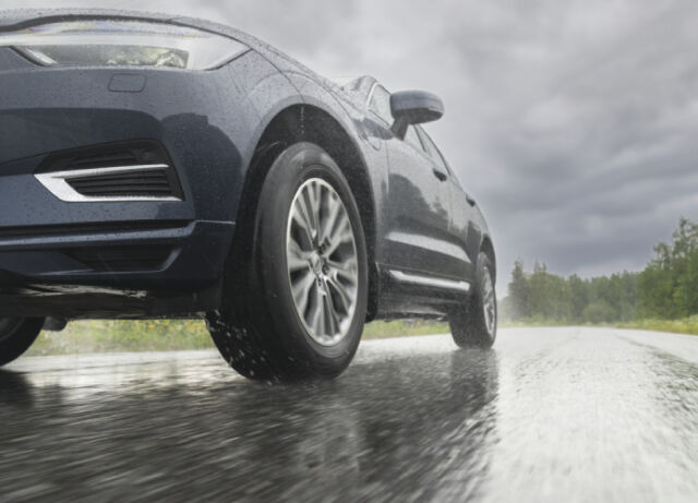 Auto läheltä kuvattuna toisesta kulmasta vesisateessa ajossa tiellä