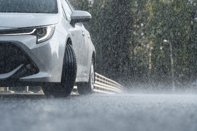 Valkoinen auto vasemmalla edestä kuvattuna vesisateessa