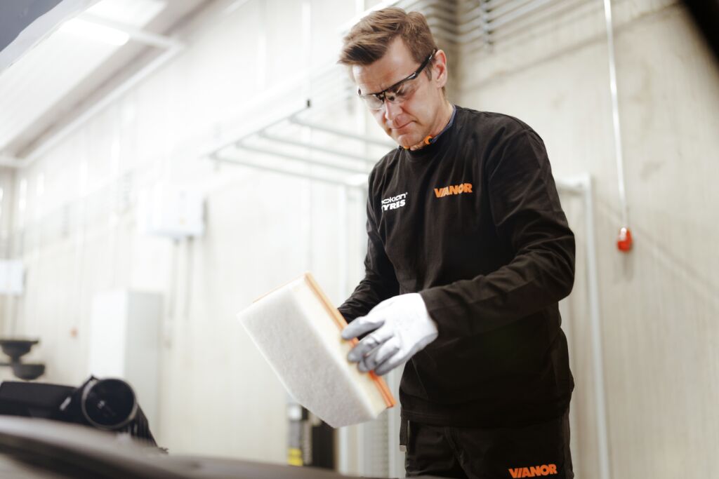Autohuollon asiantuntija tarkistamassa ilmastointilaitetta – ilmastointihuolto varmistaa auton ilmastoinnin ja kompressorin toimivuuden talvella.