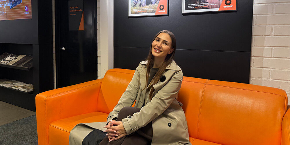 Henkilö istumassa oranssilla sohvalla uudenaikaisessa Vianorin odotustilassa, jossa on mustat seinät, valkoisia tiiliyksityiskohtia ja Vianorin brändijulisteita seinällä.