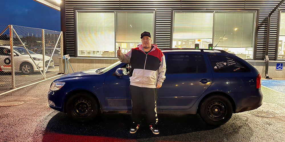 Henkilö näyttää peukkua tummansinisen farmariauton edessä Vianorin palvelupisteen ulkopuolella.